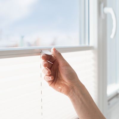 Hand an einem Plissee am Fenster